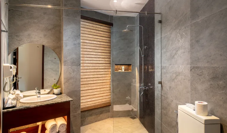Grey stone bathroom with glass shower and round mirror at Grand Serendib Hotel