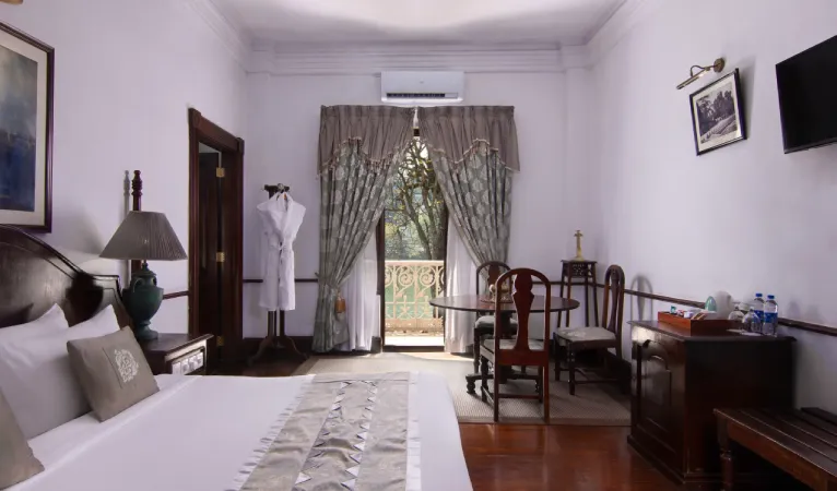Guest room at Queens Hotel Kandy with white bed, wooden furniture and a balcony door