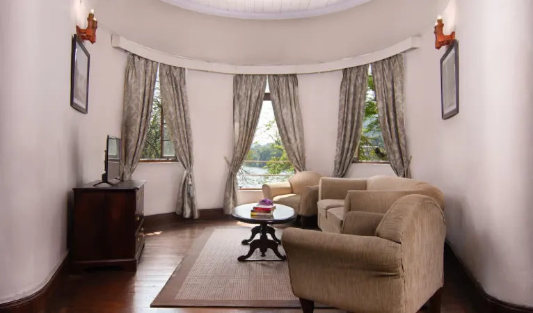 Suite sitting area with beige sofas and a bay window at Queens Hotel Kandy