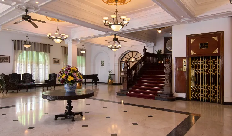 Queens Hotel lobby with chandeliers, a red-carpeted staircase and a vintage cage lift