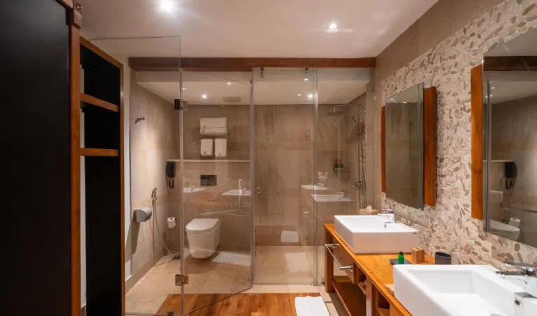 Bathroom with glass shower, stone wall and wooden vanity at The Radh Hotel