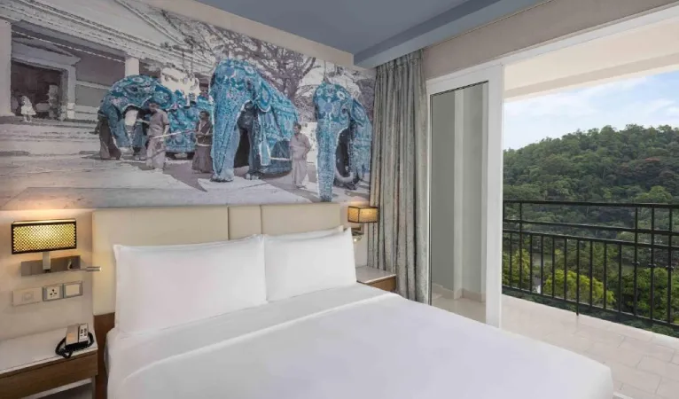 Radisson Hotel Kandy bedroom with an elephant mural above the bed and a balcony facing forested hills