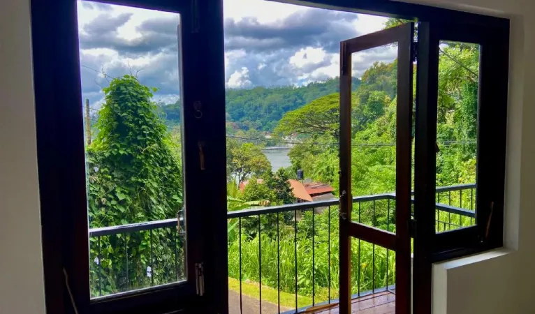 Open balcony doors with a view over trees and Kandy Lake at Sesatha Lake Kandy