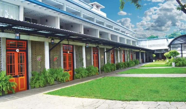 Room wing with orange doors along a lawn at Thilanka Hotel Kandy