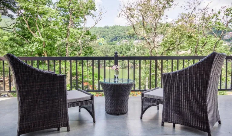 Balcony with wicker chairs overlooking trees and Kandy Lake at Viyana Boutique Hotel